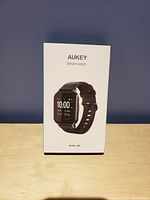 Box of Aukey LS02 smartwatch showing front image of the watch with black silicone band and digital display reading 10:00.