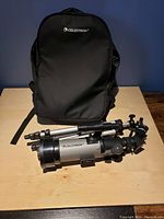 Photo of telescope, tripod, and branded carrying bag placed on table against dark background.