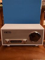 Front view of white retro Victrola radio clock showing speaker grill, knobs, frequency tuner, and large right-side dial.