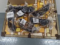 Six pairs of Condor Safety Glasses individually wrapped in clear plastic packaging, arranged on a patterned vintage fabric-covered case surface.