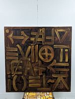 Front view of the large square painting featuring abstract shapes and symbols in gold on a brown background.