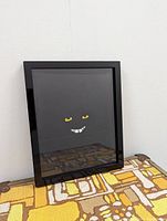 Front view of framed original artwork showing minimalist smiling face with yellow eyes and white teeth on black background.