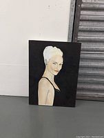 Front view of the portrait painting on canvas showing a woman with blonde hair, black dress, and blue earrings against a black background.