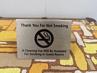 Front view of one vintage metal hotel sign featuring 'Thank You For Not Smoking' text and no smoking symbol, placed on patterned fabric.