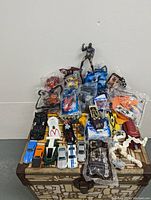 Varied vintage toys including Spiderman figure, multiple Hot Wheels cars, McDonald's toys, Lego car all arranged on a patterned suitcase.