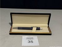 Image of a black mechanical pencil with silver clip and tip, inside a black rectangular hinged presentation case with cream interior and strap.