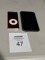 Two iPods on flat surface: red iPod Nano with click wheel and black iPod Touch with home button.