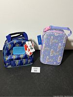 Two lunch bags side by side on a black surface with plain light background. One blue/black with animated figure design, one light purple with unicorn pattern.