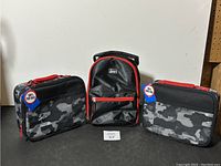 Front view of three lunch bags: two camouflage pattern lunch bags with red zippers and one black with red trim in middle.