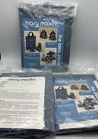 Photo shows plastic-encased blue grid plastic needlepoint canvas sheets with Mary Maxim packaging and instructions for needlepoint denim tote, accessories, and southwest craft kits.