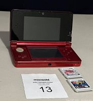 Red Nintendo 3DS handheld console open with two game cartridges in front