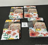 Four packaged tablecloths laid out on a black surface showing their floral designs and packaging.