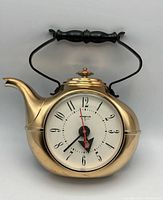 Front view of the vintage teapot-shaped Spartus wall clock showing brass-tone metal body and clock face with black handle.