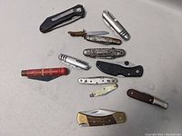 Group of 12 assorted pocket knives laid out on white surface