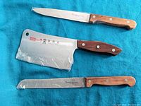 Three professional kitchen utensils laid on blue fabric with visible wooden handles and stainless steel blades.