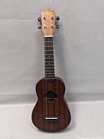Full front view of the Aleho ukulele showing the dark wood grain finish and one loose string.
