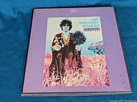 Front view of the vinyl album 'A Gift From A Flower To A Garden' by Donovan with purple cover and image of Donovan in floral outfit holding flowers and beads.