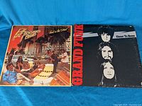 Both vinyl record covers of albums by Grand Funk and Pat Travers Band shown flat on blue fabric background.