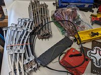 Train pieces including curved metal tracks bundled together, red transformer controller, black track switching pieces, and smaller accessories visible.