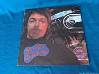 Front cover of Red Rose Speedway vinyl album showing Paul McCartney holding a rose in his mouth next to a motorcycle engine.