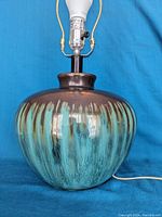 Mid-century modern table lamp showing round drip glaze ceramic base in brown and turquoise, lamp stem and socket with LED bulb.