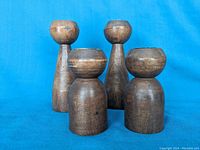 Four mid century modern wood candle holders with metal liners displayed against a blue background. Two taller, conical wood holders and two shorter, stout holders with rounded tops shown in group.