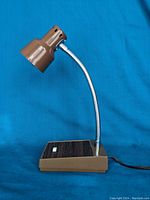 Mid century modern adjustable flex desk lamp showing lamp angle and style with brown shade and base, faux wood panel, and silver flexible neck.