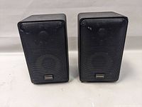 Front view of two Optimus Pro X44AV bookshelf speakers side by side showing black grille with Optimus logo on lower front.