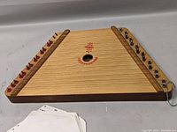Full view of wooden lap harp nepeneonoyka dulcimer with tuning pegs and strings.