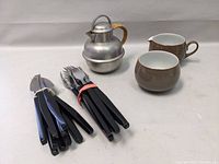 Set showing pewter teapot with wicker handle, Denby cream and sugar set and grouped cutlery