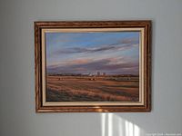 Frontal photo of the Western landscape painting showing the open fields, hay bales, and distant grain elevators under a colorful sky with wooden frame.