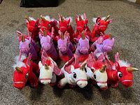 Front view showing all 15 stuffed unicorns in red, purple, and white colors arranged in rows on carpeted floor