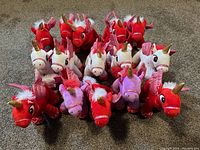 Front view of the 15 stuffed unicorns arranged in rows showing red, white, and purple colors.