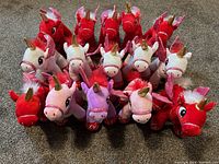 Front view of all 15 stuffed unicorn plush toys arranged on carpet floor. Colors include red, white, pink, and purple with gold horns and glittery wings.