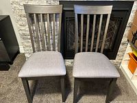 Two wood frame chairs placed side-by-side showing front view, fabric seats and slatted backrest design.