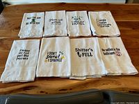All 8 white cotton hand towels laid out on table showing full embroidered text and designs