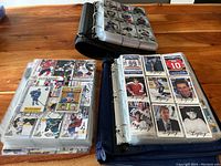 Three binders opened showing hockey and baseball sports cards organized in plastic sleeves, featuring cards like Upper Deck Legacy hockey cards with images of players and team logos.