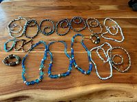 Photo showing an assortment of bracelets and necklaces on wooden surface, various bead colors and styles visible, including blue, white, brown, and speckled beads.