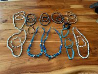 Overview of entire jewelry lot showing necklaces and bracelets in white, blue, brown, black beads and silver-tone charms on cord bracelet