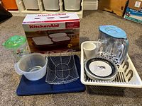 Photo showing KitchenAid 5-piece stoneware set box, Brita water pitcher with blue lid, clear container with green lid, white dish rack with cup and paper plates, mixing bowl and cooling rack.