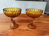 Pair of topaz gold glass compote bowls showing overall shape, scalloped rims, and amber color under natural light on wooden table.