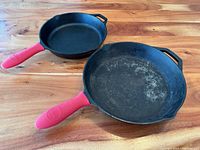 Two cast iron frying pans showing front and side views with red silicone handle sleeves.