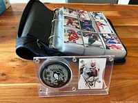 Photo showing clear acrylic case with Pittsburgh Penguins puck and Sidney Crosby signed card, binder in background