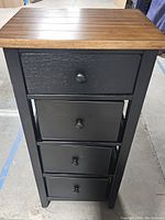 Front view of the black wooden stand showing wood top and four black drawers.
