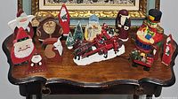 Overview of assorted holiday decorations on a wooden table, including various Santa Claus figures, small Christmas trees, and a red sled.