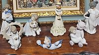 Group photo showing all seven Noa porcelain figurines arranged together on a wooden surface below framed artwork.