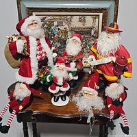 Seven Santa Claus figurines arranged on a wooden table with a framed picture in the background.