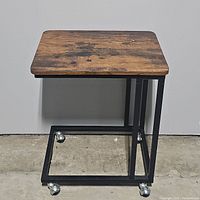 Front view of rolling side table showing wooden top and black metal frame with caster wheels.