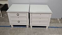 Pair of white night stands photographed side-by-side showing front and top view with glass tops.