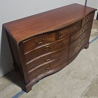 Full perspective view of the nine drawer dresser, showcasing the curved front and dark brown finish.